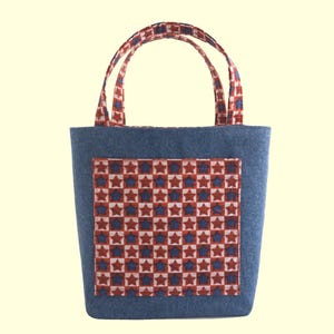 May include: A denim tote bag with a rectangular pocket featuring a red, white, and blue star pattern. The handles and pocket trim have a matching star design. The bag is designed for carrying items.