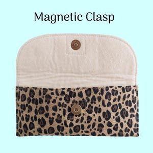 Puede incluir: Un bolso de mano con estampado de leopardo en el exterior y un interior color crema. El bolso tiene un cierre magn&eacute;tico. El texto "Magnetic Clasp" se muestra en la parte superior de la imagen. El bolso est&aacute; abierto, revelando el interior.