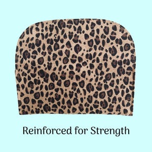 Puede incluir: Una tela con estampado de leopardo con manchas marrones y negras sobre un fondo beige. La tela est&aacute; curvada en la parte superior y tiene el texto "Reinforced for Strength" en la parte inferior. El fondo es azul claro.