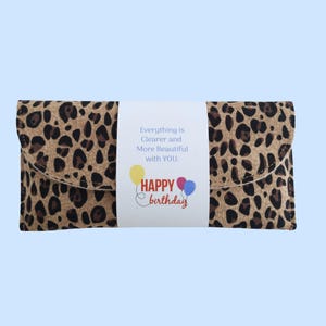 Puede incluir: Un bolso de mano con estampado de leopardo con una banda blanca con el texto "Everything is Clearer and More Beautiful with YOU." Debajo, "Happy Birthday" con gr&aacute;ficos de globos. El bolso es rectangular con solapa.