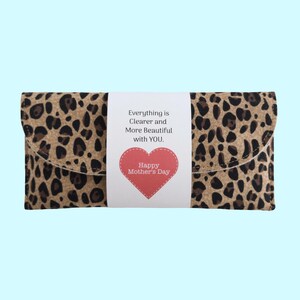 Puede incluir: Un bolso de mano con estampado de leopardo con una banda blanca con el texto "Everything is Clearer and More Beautiful with YOU". Un coraz&oacute;n rojo con "Happy Mother's Day" tambi&eacute;n est&aacute; en la banda.
