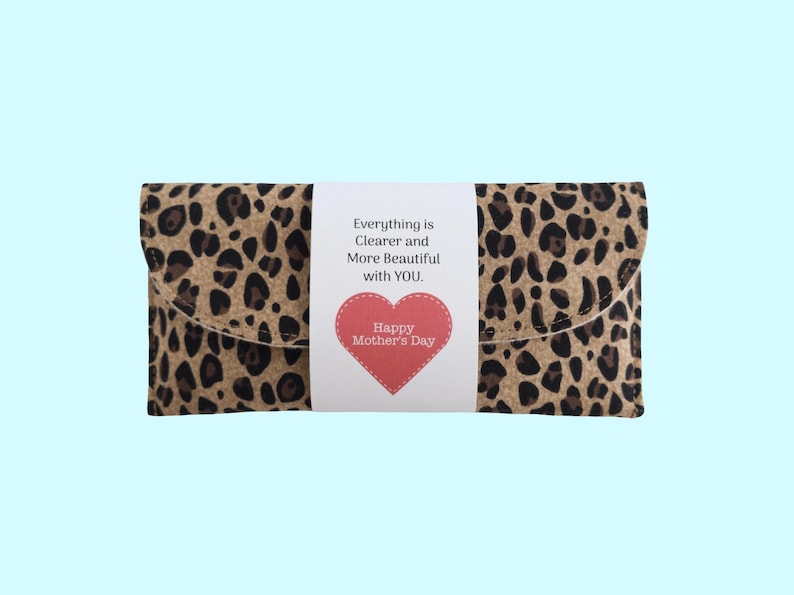 Puede incluir: Un bolso de mano con estampado de leopardo con una banda blanca con el texto "Everything is Clearer and More Beautiful with YOU". Un coraz&oacute;n rojo con "Happy Mother's Day" tambi&eacute;n est&aacute; en la banda.