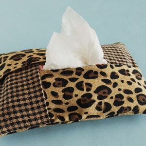 May include: A brown and black leopard print tissue box cover with a checkered pattern on the side. The cover has a white tissue peeking out of the opening.