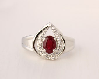 Op de afbeelding: Een zilveren ring met een traanvormige zetting met een rode robijn omringd door een halo van kleinere witte stenen.