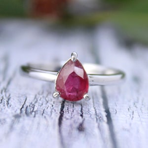 Peut inclure: Une bague en argent avec une pierre précieuse en rubis de forme poire. La bague est simple et élégante, avec une bande délicate.