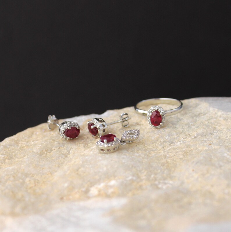 K&ouml;nnte beinhalten: Ein Schmuckset aus Rubin und Diamant mit einem Ring, Ohrringen und einem Anh&auml;nger. Der Schmuck ist in Silber gefasst und zeigt rote Rubin-Edelsteine, die von funkelnden Diamanten umgeben sind.