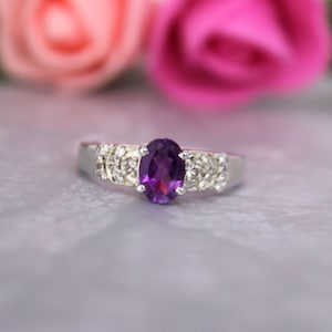 May include: A silver ring with a large oval amethyst gemstone surrounded by smaller clear gemstones.