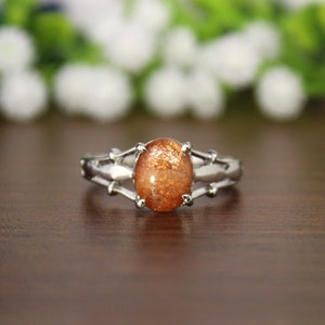 May include: A silver ring with a large oval-shaped sunstone gemstone. The stone is a warm orange color with flecks of gold.