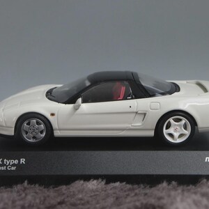 May include: A white Honda NSX Type R model car with a black roof and red interior. The miniature car is displayed on a black base with text that reads "Honda NSX type R Nürburgring Test Car". The model car is a collectible.