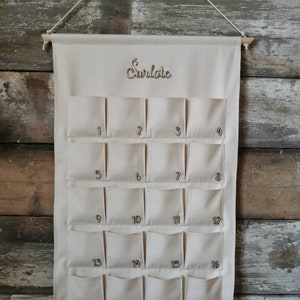Personalized canvas advent calendar which can be used again every year. Featuring 24 pockets to mark each day of December it can be filled with small gifts. Off white, sand, ecru colors. Custom handmade product with wooden numbers gift box for kids.