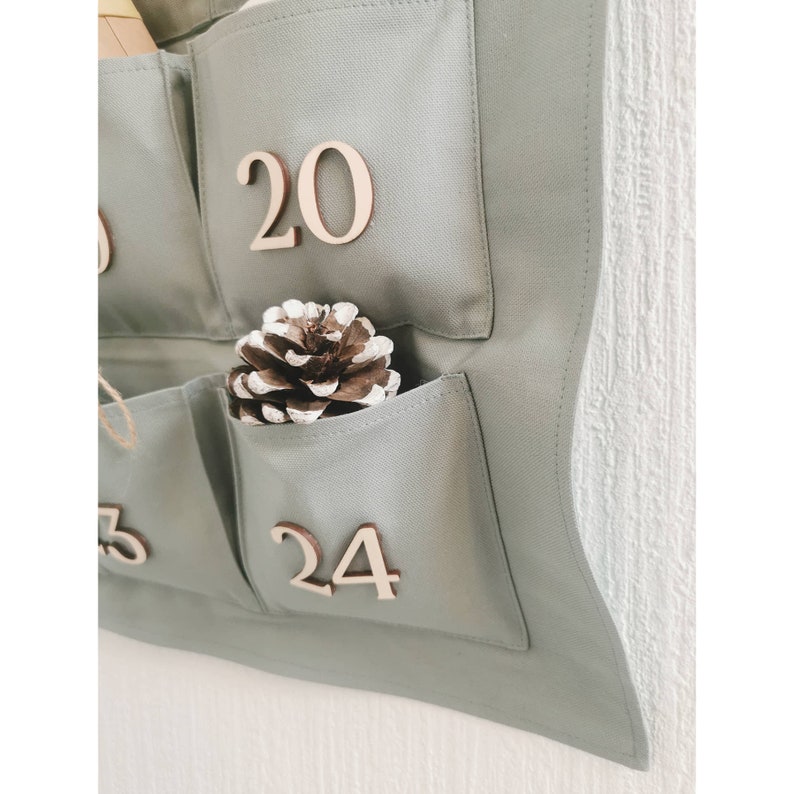 Canvas personalized advent calendar which can be used again every year. Featuring 24 pockets to mark each day of December it can be filled with small gifts. Sage, old green colors. Handmade product. With wooden numbers. Custom order gift box for kids