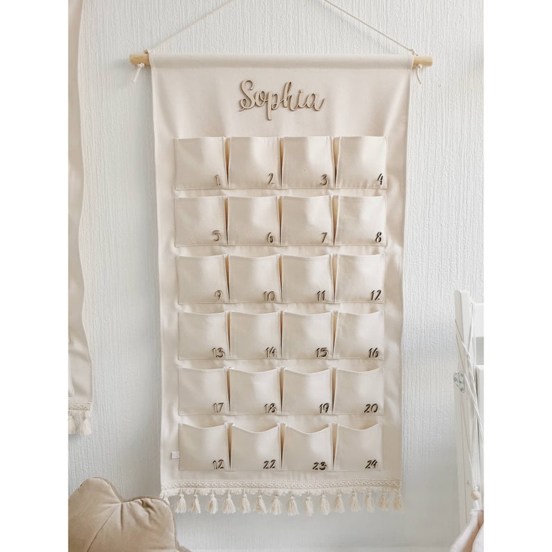 Personalized canvas advent calendar which can be used again every year. Featuring 24 pockets to mark each day of December it can be filled with small gifts. Off white, sand, ecru colors. Custom handmade product with wooden numbers gift box for kids.