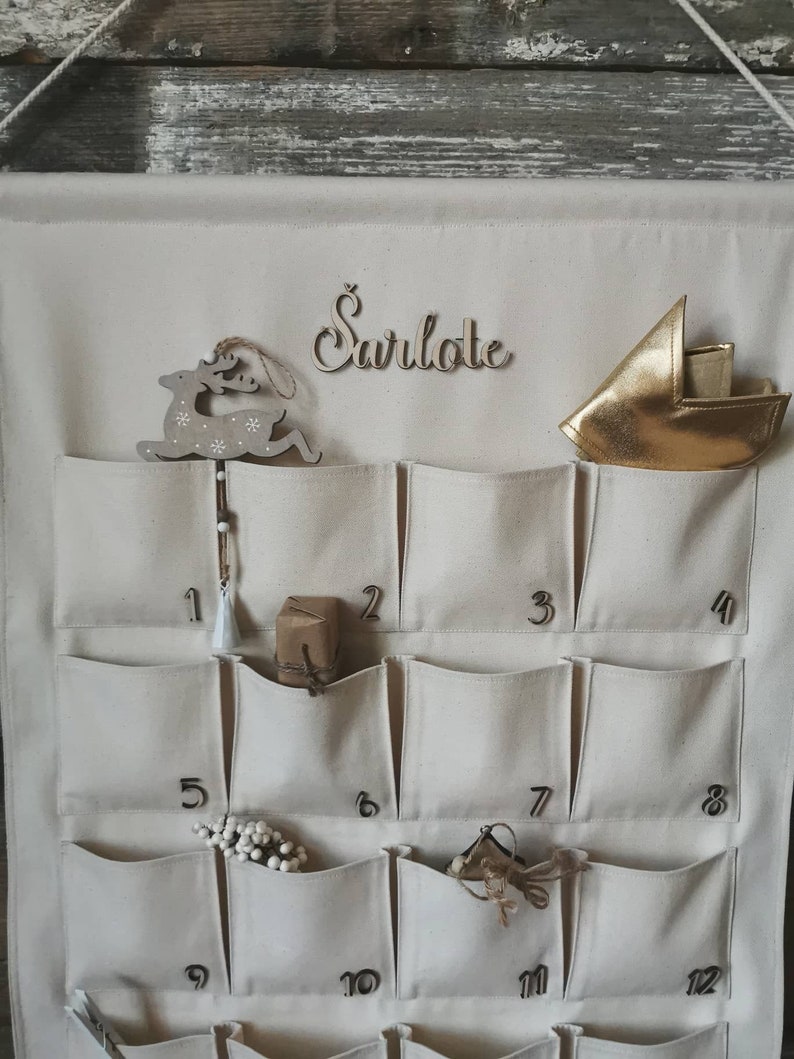 Countdown to Christmas with this canvas advent calendar which can be personalized with name. Featuring 24 pockets to mark each day of December, it can be filled with small gifts. Off white, sand, ecru colors. Handmade product. With wooden numbers.
