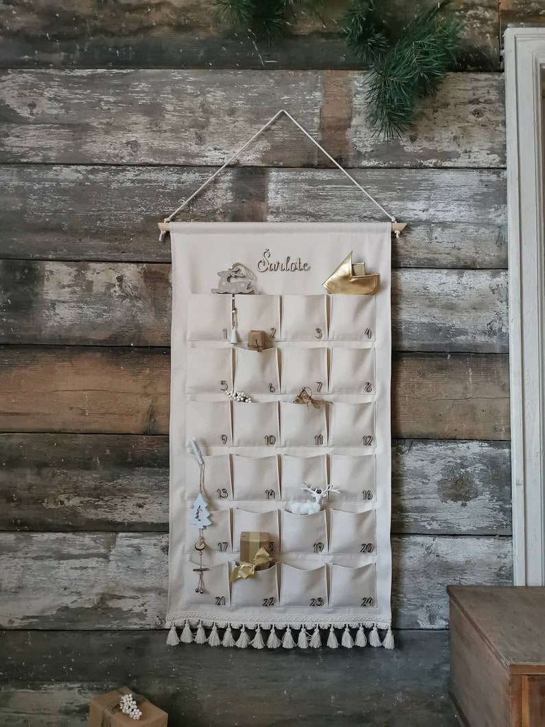 Personalized canvas advent calendar which can be used again every year. Featuring 24 pockets to mark each day of December it can be filled with small gifts. Off white, sand, ecru colors. Custom handmade product with wooden numbers gift box for kids.