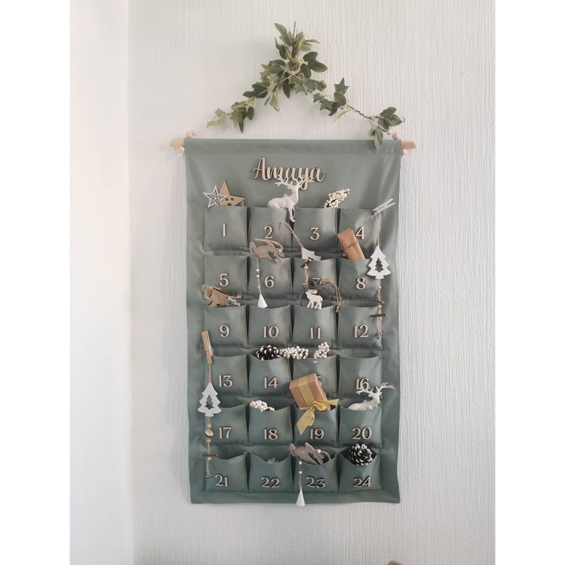 Canvas personalized advent calendar which can be used again every year. Featuring 24 pockets to mark each day of December it can be filled with small gifts. Sage, old green colors. Handmade product. With wooden numbers. Custom order gift box for kids