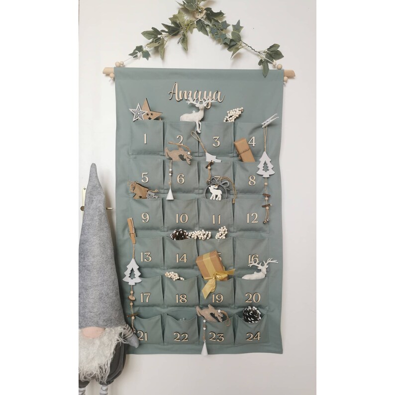 Canvas personalized advent calendar which can be used again every year. Featuring 24 pockets to mark each day of December it can be filled with small gifts. Sage, old green colors. Handmade product. With wooden numbers. Custom order gift box for kids