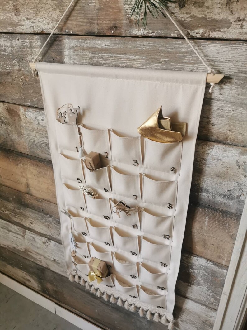 Countdown to Christmas with this canvas advent calendar, which can be used again  every year. Featuring 24 pockets to mark each day of December, it can be filled with small gifts. Off white, sand, ecru colors. Handmade product. With wooden numbers.