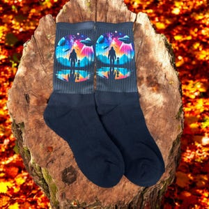 May include: A pair of black socks with a colorful design featuring a silhouette of Bigfoot and an alien walking through a forest with a starry sky and flying saucers in the background.
