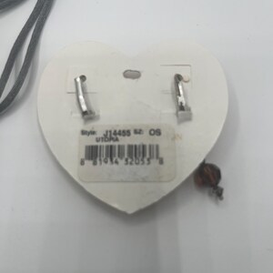 May include: A pair of silver-tone earrings with a heart-shaped backing. The earrings have a small, dangling bead. The backing has a sticker with the style number J14455 and the word UTOPIA.