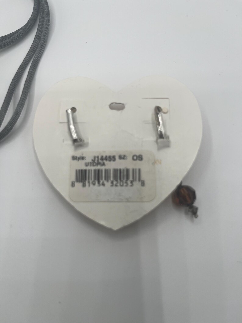 May include: A pair of silver-tone earrings with a heart-shaped backing. The earrings have a small, dangling bead. The backing has a sticker with the style number J14455 and the word UTOPIA.