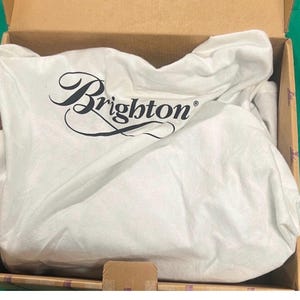 May include: A white dust bag with the word "Brighton" in black script is inside a cardboard box. The bag is crumpled and appears to be made of a soft fabric. The box is open, revealing the contents.