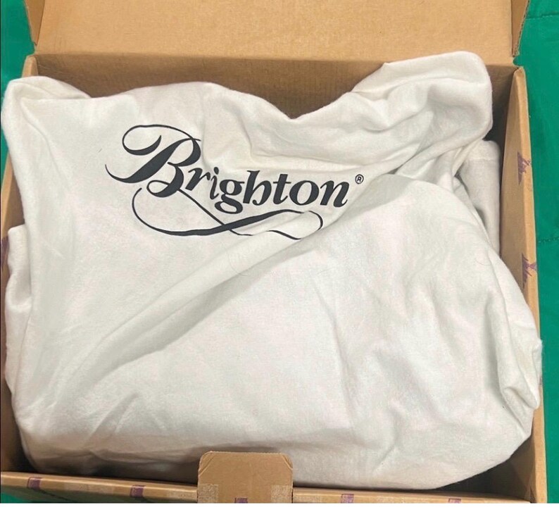 May include: A white dust bag with the word "Brighton" in black script is inside a cardboard box. The bag is crumpled and appears to be made of a soft fabric. The box is open, revealing the contents.