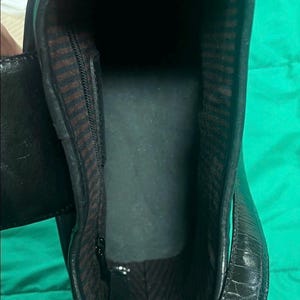 May include: Black leather boot interior with a zipper and brown and black striped lining. The boot has a textured exterior and a dark interior. The image is taken from an overhead perspective.