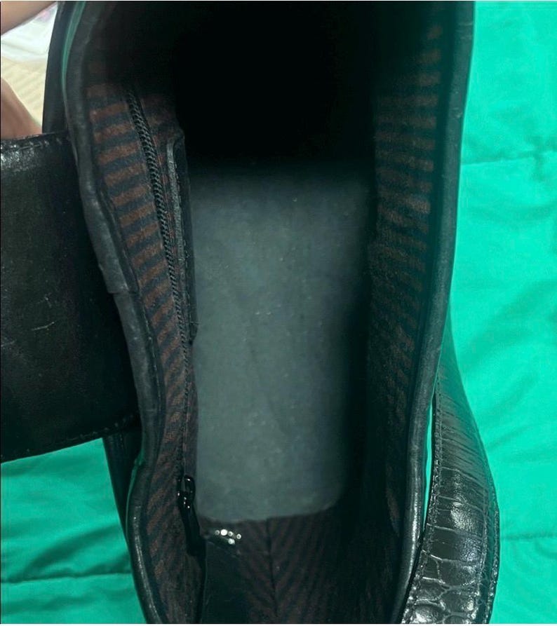 May include: Black leather boot interior with a zipper and brown and black striped lining. The boot has a textured exterior and a dark interior. The image is taken from an overhead perspective.