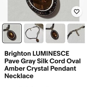 May include: An oval amber crystal pendant necklace with a gray silk cord. The pendant is surrounded by a silver-toned frame with small, dark-colored stones. The necklace is from Brighton.