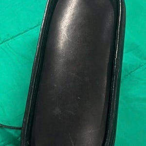 May include: A black, rectangular eyeglasses case with a rounded top. The case is made of a smooth, leather-like material and has a black frame. The case is empty.
