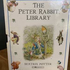 May include: The Peter Rabbit Library box set featuring illustrations of Peter Rabbit and other characters. The box is white with blue trim and includes the text "The Peter Rabbit Library" and "Beatrix Potter". The box has illustrations of a squirrel, a duck, and other animals.