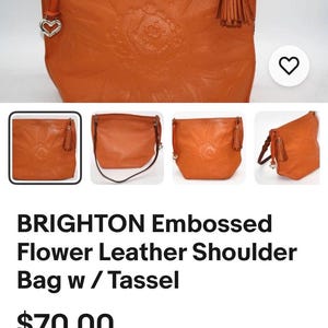 May include: An orange shoulder bag featuring an embossed floral pattern on the front, a matching leather tassel attached to the side, and a silver-toned heart-shaped charm hanging from a strap. The bag has a structured shape and a smooth finish.