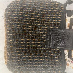 Puede incluir: Bolso tejido con un patr&oacute;n negro y beige. El bolso presenta una solapa y una correa negras texturizadas. El forro interior es visible, mostrando un dise&ntilde;o floral. Un accesorio elegante.