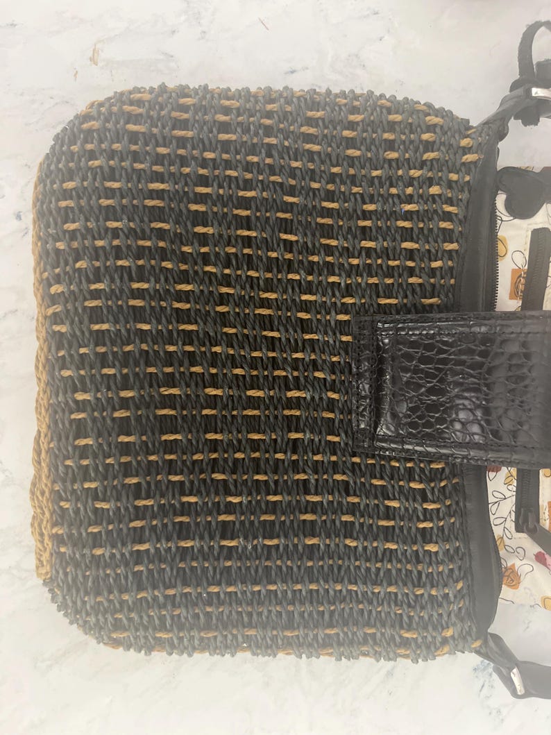 Puede incluir: Bolso tejido con un patr&oacute;n negro y beige. El bolso presenta una solapa y una correa negras texturizadas. El forro interior es visible, mostrando un dise&ntilde;o floral. Un accesorio elegante.