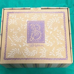 May include: A rectangular cardboard box with a beige background and a purple border. The box features a central purple square with a stylized letter "B" and the word "Brighton" in a script font. The box is decorated with white floral and vine patterns.