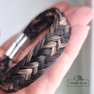May include: A braided horsehair bracelet with black, brown, and blonde strands. The bracelet has a silver clasp.