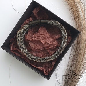 May include: A braided horsehair bracelet with a black metal clasp. The bracelet is in a black box with brown tissue paper.