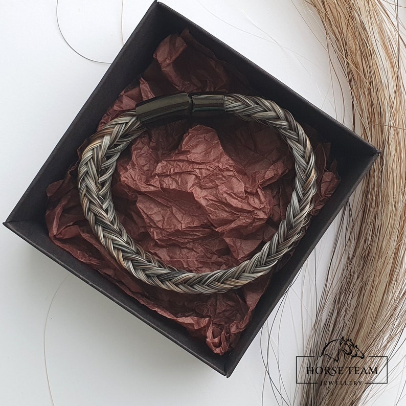 May include: A braided horsehair bracelet with a black metal clasp. The bracelet is in a black box with brown tissue paper.
