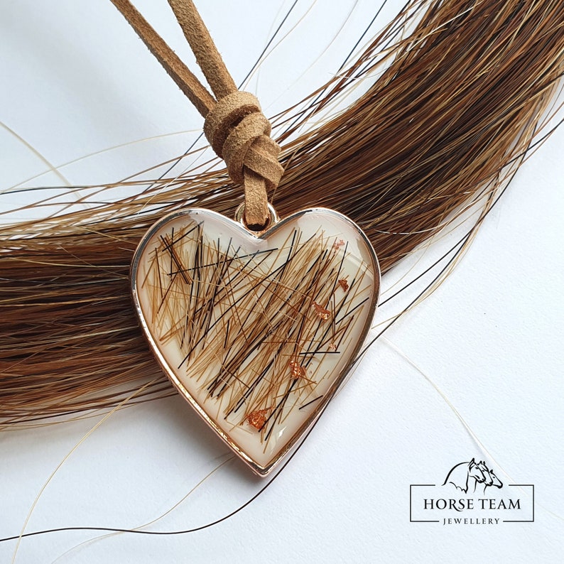 May include: A heart-shaped pendant necklace with a brown suede cord. The pendant is filled with brown horse hair and gold glitter.