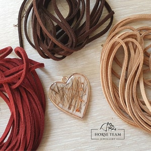 May include: A heart-shaped pendant with a gold-colored frame filled with brown horse hair. The pendant is surrounded by three spools of suede cord in red, brown, and tan.
