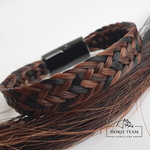 May include: A braided bracelet made from brown and black horsehair with a black metal clasp. The bracelet is shown on a background of loose horsehair. The text "HORSE TEAM JEWELLERY" is visible in the lower right corner of the image.