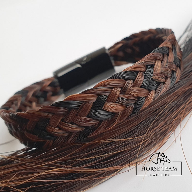 May include: A braided bracelet made from brown and black horsehair with a black metal clasp. The bracelet is shown on a background of loose horsehair. The text "HORSE TEAM JEWELLERY" is visible in the lower right corner of the image.