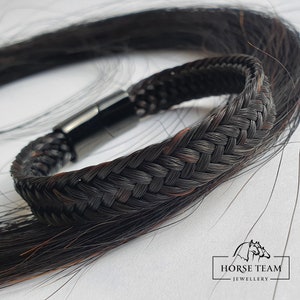 May include: A black braided horsehair bracelet with a black magnetic clasp. The bracelet is made with a woven pattern and is a unique piece of jewelry.