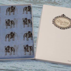 May include: A blue silk scarf with a repeating pattern of brown bulldogs. The scarf is packaged in a white box with the text "The Branding House" and "Hand Printed in the UK".