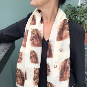 Puede incluir: Una bufanda blanca con estampado de caballo marr&oacute;n y detalles de herradura. La bufanda est&aacute; hecha de un tejido suave y ligero, perfecta para a&ntilde;adir un toque de estilo a cualquier atuendo.