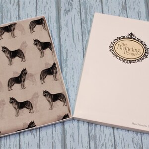 May include: A rectangular gift box containing a light beige fabric featuring a repeating pattern of dark grey husky dogs. The box lid is white with a decorative black oval frame containing the text The Branding House and Hand Printed In The UK.