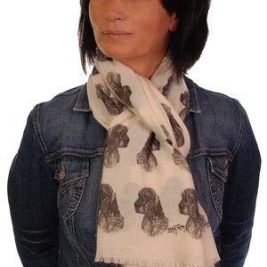 May include: A woman wearing a denim jacket over a white scarf with a brown and white dog print. The scarf has a fringe edge and the dog print is repeated throughout the scarf.