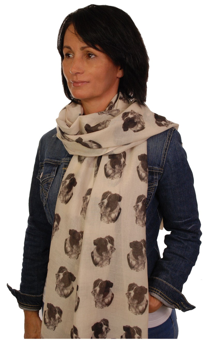 May include: A woman wearing a denim jacket and a white scarf with a repeating pattern of black and white border collie dog faces.