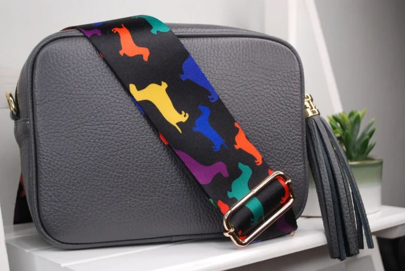 May include: A gray leather crossbody bag with a black and rainbow patterned strap and a gray leather tassel.