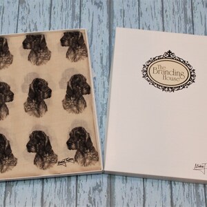 May include: A beige scarf with a repeating pattern of black and white dog illustrations. The scarf is in a white box with a label that says "The Branding House".